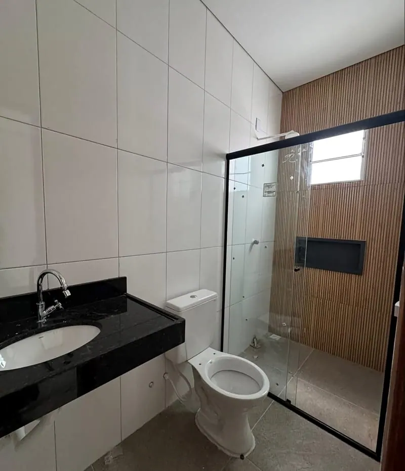Banheiro da casa, com box de vidro, pia de granito e painel de madeira