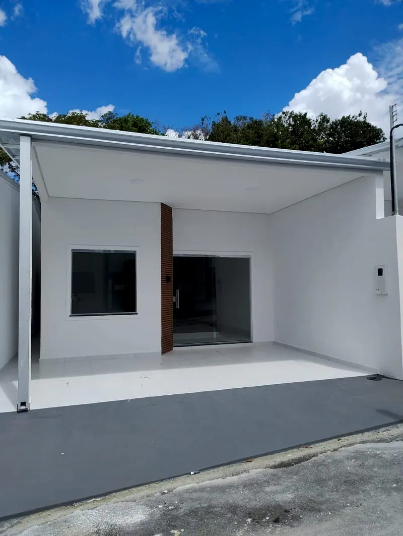 Frente da casa de 2 quartos em residencial fechado, com a garagem coberta, o painel de madeira e o céu azul