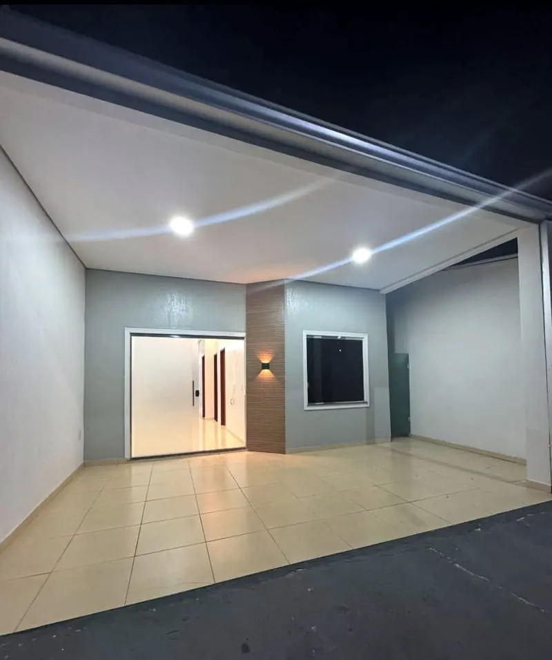 Garagem coberta da casa à noite, com as luzes acesas e a porta de entrada