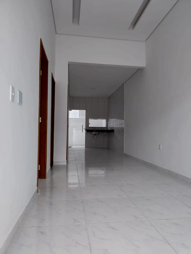 Sala e corredor da casa, com piso claro e a cozinha ao fundo