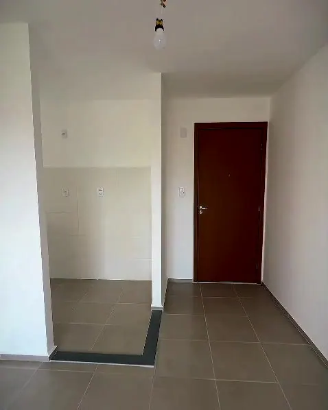 Sala do apartamento, vazia, com a cozinha à esquerda e a porta de entrada ao fundo